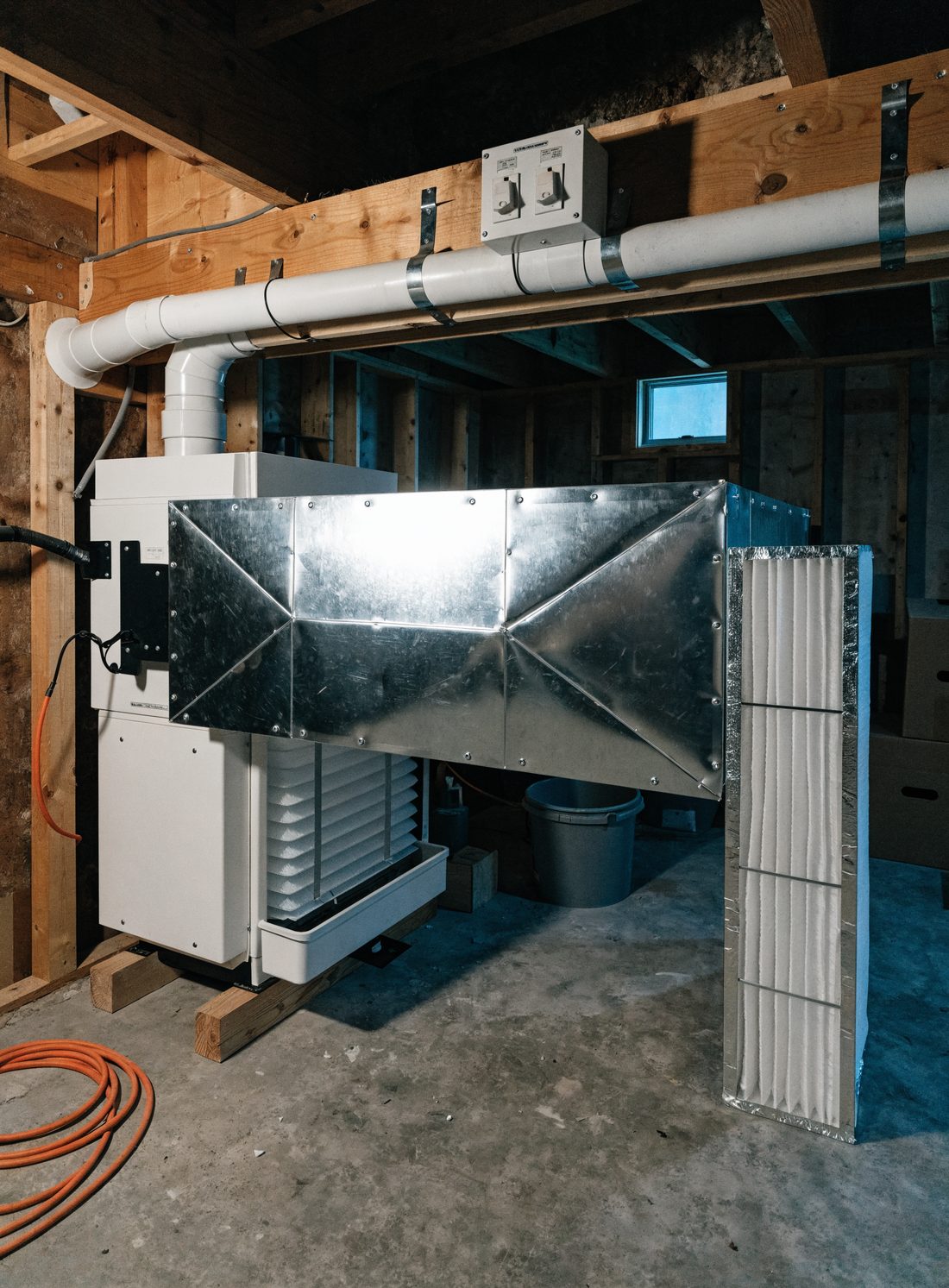 A newly installed furnace and coil in a basement, with folded sheet metal plenum work, white PVC venting run to the rim joist and a labelled disconnect box on the joist